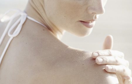 Femme s'appliquant de la crème sur l'épaule droite